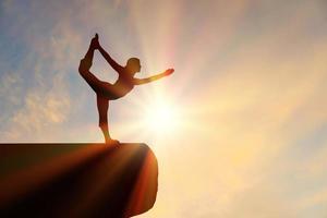 Portrait-Silhouette-Frauen machen Yoga auf Silhouette-Stein mit einem ruhigen orangefarbenen Sonnenuntergang. foto