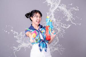 Eine schöne asiatische Frau zeigt eine Geste, während sie während des Songkran-Festivals eine Wasserpistole aus Kunststoff hält foto