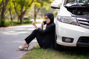eine junge asiatin ruft ihren servicetechniker an, um ein kaputtes auto am straßenrand zu reparieren foto