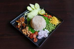 thailändisches Essen - Reis gemischt mit Garnelenpaste, Kao cluk ka pi mit Beilage als Mango, Zitrone, Chili, Gurke, Rührei, Kuherbse, Schalotten, chinesischer Wurst, getrockneten Garnelen und Schweinefleisch foto