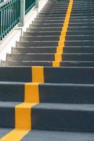 die Treppe der Überführung mit gelber Fahrbahnlinie und Geländer zur Sicherheit beim Überqueren der Straße. Wegzeichen auf der Leiter. gelbes kreuz auf der treppe.