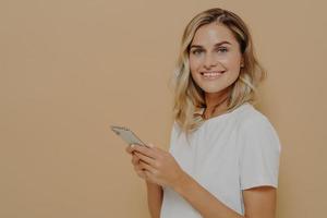 Porträt einer fröhlichen jungen Frau in weißem T-Shirt, die glücklich ist, gute Nachrichten auf dem Smartphone zu lesen foto
