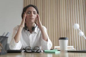 Frustrierte italienische Frau mit geschlossenen Augen, die Schläfen massiert und unter Kopfschmerzen bei der Arbeit leidet