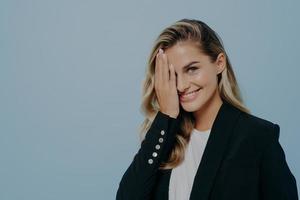 schüchternes blondes Mädchen, das die Hälfte ihres Gesichts mit der Hand bedeckt foto