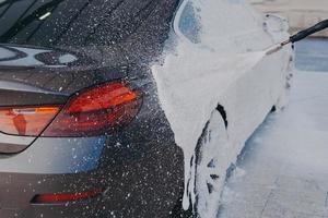 Autoaußenreinigung, Auftragen von Schneeschaum auf die schmutzige Autooberfläche aus dem Hochdruckreiniger