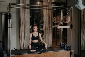 junge sportliche Frau, die in sehr entspannter Lotusposition auf der Pilates-Maschine sitzt foto