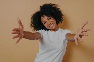 Fröhliche, freundliche afroamerikanische Frau in weißem Hemd, die Umarmungen anbietet und den Kunden willkommen heißt foto