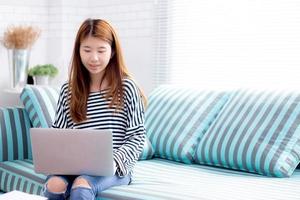 schöne Porträt junge asiatische Frau mit Laptop für die Freizeit auf dem Sofa im Wohnzimmer, Mädchen arbeitet online mit Notebook freiberuflich mit einem glücklichen Kommunikationsgeschäftskonzept. foto