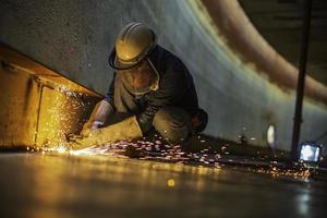 männlicher arbeiter metallschneidender funke auf der stahlplatte des tankbodens mit blitz des schneidlichtes nahaufnahme tragen schutzhandschuhe und maske foto