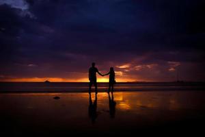 Silhouette eines Paares halten sich an der Hand und ein glückliches junges Paar liebt sich bei Sonnenuntergang am Strand foto