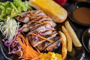 Schweinesteak mit Brot, Karotten, Blumenkohl, Salat und Mais auf einem schwarzen Teller. foto