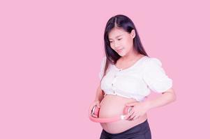eine schöne schwangere asiatin steht entspannt da und lässt ihr ungeborenes kind musik mit kopfhörern hören, die mit dem internet verbunden sind