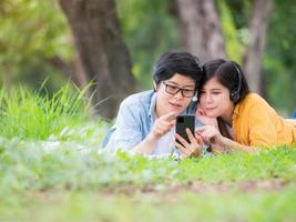 asiatische lgbt-paare entspannen sich im park und hören musik auf ihren handys foto