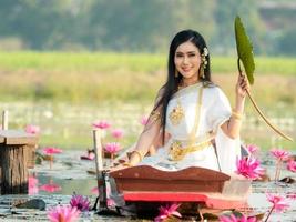 eine elegante thailändische frau, die traditionelle thailändische kleidung trägt und lotusblumenblätter trägt, die von einem lotusfeld gesammelt wurden foto