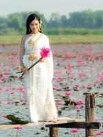 Eine elegante thailändische Frau, die traditionelle thailändische Kleidung trägt und Lotusblumen trägt, die von einem Lotusfeld gesammelt wurden foto