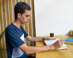 junger mann mit schwarzen haaren, der ein buch liest, teenager in lässiger kleidung in der bibliothek foto