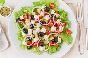 griechischer salat auf weißer platte auf altem rustikalem weißem holztisch, frischer salat