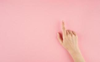 schöne Frauenhand, die auf etwas auf rosa Hintergrund mit Draufsicht des Kopienraums berührt oder zeigt foto
