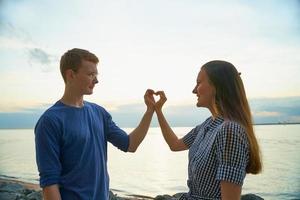 Liebesgeschichte von zwei, Jungen und Mädchen, die Herz mit Fingern machen, Strandhintergrund foto