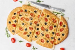Focaccia, Pizza mit Tomaten, Oliven und Rosmarin. Stück italienisches Fladenbrot. Ansicht von oben foto