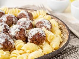 Schwedische Fleischbällchen mit Fusilli-Paste auf weißem Holztisch, Teil des Tellers, Seitenansicht foto