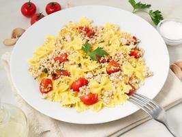 Farfalle-Nudeln mit Tomaten, Hühnerfleisch, Petersilie auf weißem Steinhintergrund, kalorienarme Ernährung, Seitenansicht