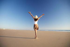 glückliche Frau mit Hut, der am Strand geht