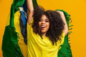 Afro-Mädchen jubelt der brasilianischen Lieblingsmannschaft zu und hält die Nationalflagge auf gelbem Hintergrund. foto