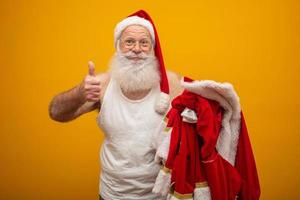 der weihnachtsmann hält seine kleidung nach oder vor der lieferung von geschenken. die kleidung des weihnachtsmanns. Kostüm. Daumen hoch. foto