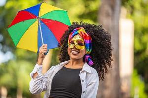 junge lockige haarfrau, die die brasilianische karnevalsparty mit frevo-regenschirm auf der straße feiert. foto