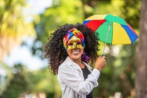 junge lockige haarfrau, die die brasilianische karnevalsparty mit frevo-regenschirm auf der straße feiert. foto