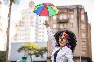 junge lockige haarfrau, die die brasilianische karnevalsparty mit frevo-regenschirm auf der straße feiert. foto