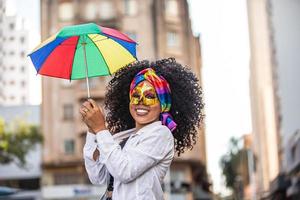 junge lockige haarfrau, die die brasilianische karnevalsparty mit frevo-regenschirm auf der straße feiert. foto