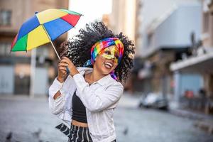 junge lockige haarfrau, die die brasilianische karnevalsparty mit frevo-regenschirm auf der straße feiert. foto