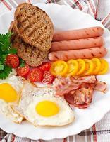 Englisches Frühstück - Spiegeleier, Speck, Würstchen und geröstetes Roggenbrot foto