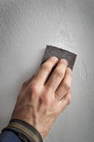 männliche Hand, die etwas Sandpapier gegen eine Wand hält foto