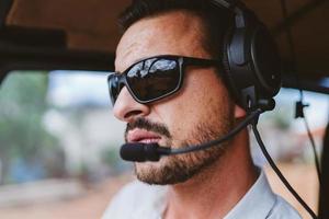 Pilot mit Headset, der Kontrollen in einem privaten Hubschrauber einleitet. Hubschrauberpilot sitzt im Cockpit. lateinischer Mann. foto