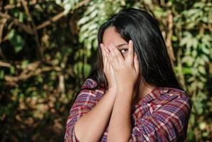 Verspielte schüchterne Frau, die das Gesicht versteckt und schüchtern lacht. süße Teenager-Mädchen lächelnd glücklich durch die Hände. Naturhintergrund. foto