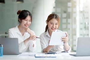 zwei junge asiatische geschäftsfrauen diskutieren die arbeits- und planungsstrategie für investitionsprojekte. geschäftsleute, die zusammen mit laptop-computer im büro sprechen. foto