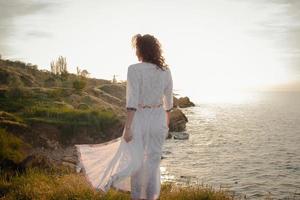 junge frau, die in einem schönen weißen kleid am morgenstrand spazieren geht. fitte frau, die sich während des aufgangs des sonnenaufgangs gut amüsiert. foto