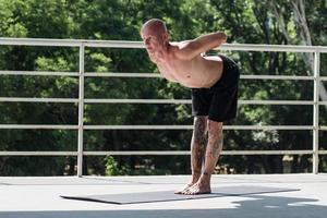 junger Mann mit Tätowierungen macht Yoga-Übungen im Freien auf dem Balkon foto