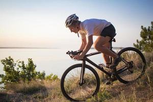 Fahrradfahrer auf professionellem Cyclocross-Rad fahren bergab, Kiefern- und Seehintergrund foto