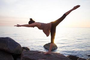 asiatische frau der fitness gemischten rasse in yoga-pose am morgenstrand, schöne fitte frau übt fitness exrxise steine, morgenmeer oder ozean hintergrund foto