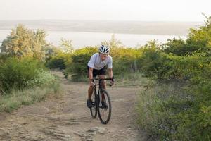 Fahrradfahrer auf professionellem Cyclocross-Rad fahren bergab, Kiefern- und Seehintergrund foto