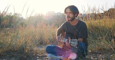 junge gutaussehende männliche spielen in der akustischen gitarre am strand an sonnigen tagen, im meer oder im ozean im hintergrund foto