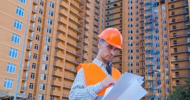 Porträt des Baufachmanns in orangefarbenem Helm und Sicherheitsweste gegen großes Gebäude foto
