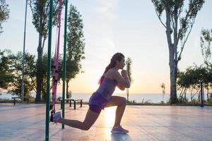 schöne fitte frau in rosa und lila sportbekleidung morgens training im outdoor-fitnessstudio, übungen mit aufhängungsgurten im park foto