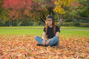 junge Frau mit roten Dreadlocks und Brille, die sich im Herbstpark entspannt foto