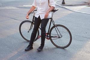 junger bärtiger mann mit lederrucksack, der mit schwarzem fahrrad geht foto