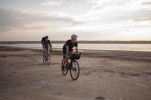 Zwei junge Männer auf einem Tourenrad mit Rucksäcken und Helmen in der Wüste auf einer Fahrradtour foto